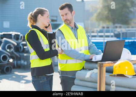 workers looking at laptop leaned on building materials Stock Photo