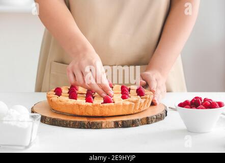 Woman decorating tasty pie with raspberry on table, closeup Stock Photo