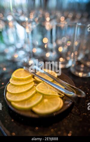 Lemon slices in a black plate are placed on a granite bar counter. Many water and wine glasses backgrounds create beautiful bokeh, elegant and romanti Stock Photo