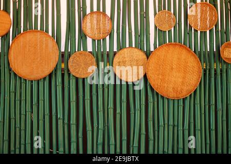 A wall made from green bamboos, decorated with round weaved bamboo plates. Stock Photo