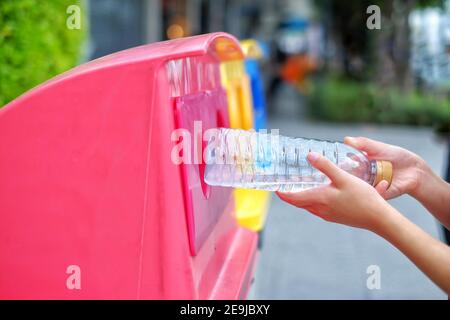A close up picture of a cute young Asian girl throwing away an empty plastic water bottle on a recycling bin which sorted waste into 3 groups, recycla Stock Photo