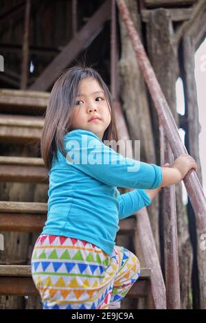 A cute young Asian girl is playing at a playground, climbing up a flight of stairs to a slide above. Stock Photo