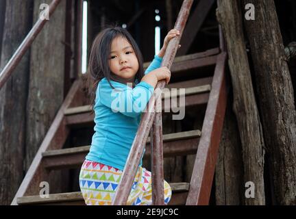 A cute young Asian girl is playing at a playground, climbing up a flight of stairs to a slide above. Stock Photo