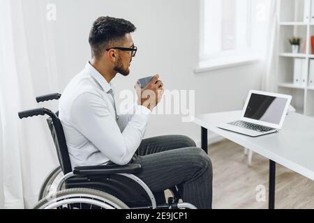 Disabled young businessman drinking coffee at his working table Stock Photo