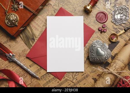 Vintage Love Card on Top of Red Envelope Mockup with retro elements like wax seal and stamp, feather pen, heart box, ribbon, medallion, vintage sheets Stock Photo