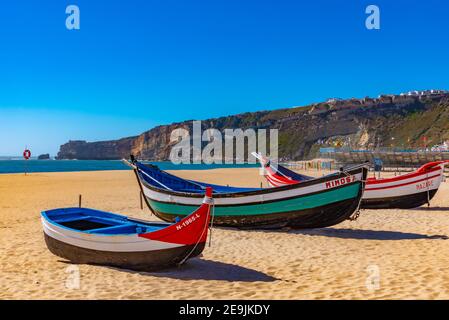 close up of traditional vintage wooden fishing boat on main beach of  village of Nazare.The high cliff of Nazare Sitio and its lighthouse on  background. Nazare, in Portugal Stock Photo