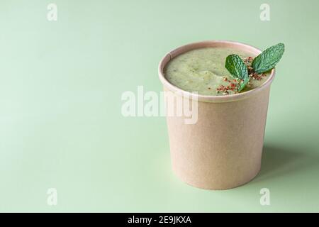 Vegetarian green cream soup in craft container for take away food decorated with mint and spices. Ecological individual package. Delivery concept. Sel Stock Photo