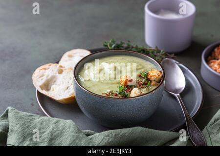 Broccoli cream soup decorated with thyme, cream, roasted cauliflower and fresh bread on green concrete background. Healthy vegetarian food concept. Se Stock Photo