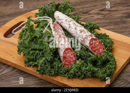 Spanish Fuet sausage with salad leaves over wooden background Stock Photo