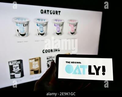 Person holding cellphone with logo of Swedish vegan food company (oat products) Oatly AB on display in front of homepage. Focus on cellphone screen. Stock Photo