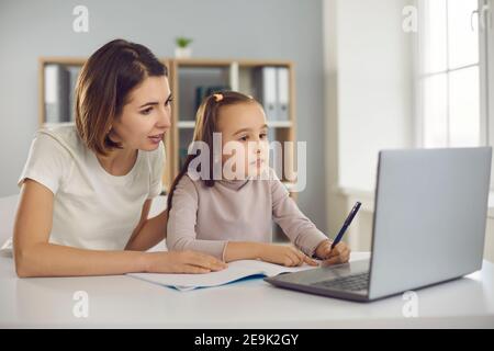 Mother and small girl daughter sitting together and making homework or tasks during online lesson Stock Photo