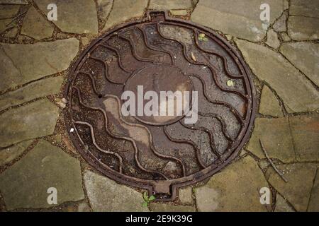Old manhole with letter k wet after rain. Stock Photo
