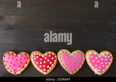 Row of lovely heart shaped polka dots royal icing cookies on black wooden background Stock Photo