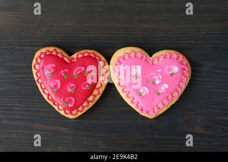 Pair of heart shaped flower pattern royal icing cookies Isolated on black wooden background Stock Photo