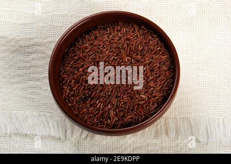 Wooden chopsticks and raw red rice in a clay bowl on a light fabric background. uncooked brown wild rice, top view Stock Photo