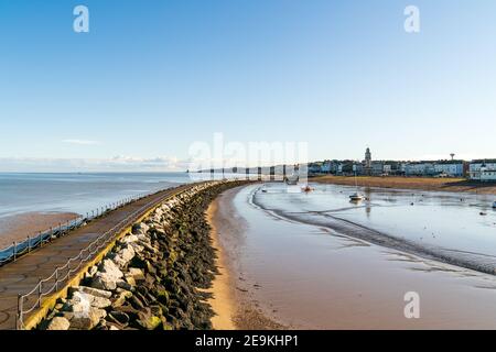 The harbour jetty at Herne Bay in Kent. View from the end of the pier looking along the sea and harbour as the jetty sweeps gently around to the coastal town on a winter's day with a blue sky. Low tide. Stock Photo