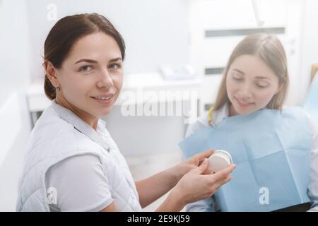 Young female dentist smiling to the camera while working with a patient Stock Photo