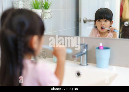 Asian cute child girl or kid brushing her teeth by toothbrush in the bathroom. Dental hygiene Healthcare concept. Stock Photo