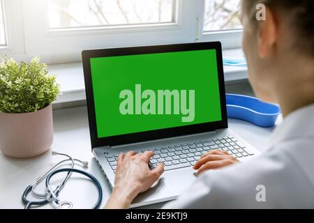 female doctor typing on her laptop computer in medical clinic office. blank green screen mockup Stock Photo