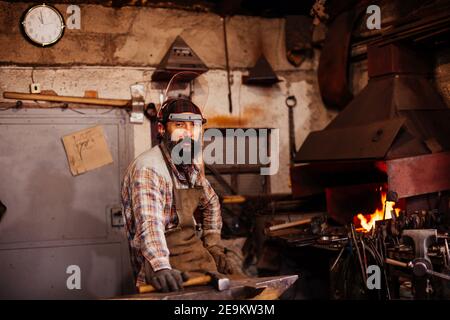 Bearded blacksmith after working in his workshop. Blacksmith's workshop. Stock Photo