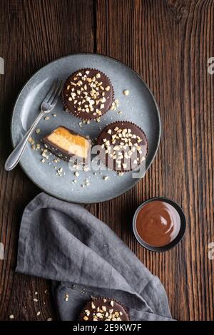 Cold crunchy treat, chocolate cups with caramel and peanut butter filling, sprinkled with chopped nuts on rustic wooden background Stock Photo