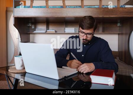 Focused serious male student using laptop looking at computer screen typing e-learning internet course , thinking and preparing for test exam doing pr Stock Photo
