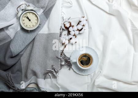 Cozy morning. Breakfast in bed. White and gray bedding, plaid and coffee cup, alarm clock. Stock Photo