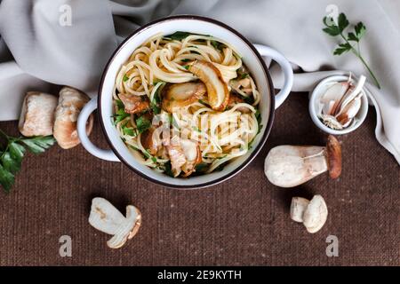 Pasta with fresh porcini mushrooms and parsley in a white vintage pot on a brown tablecloth Stock Photo