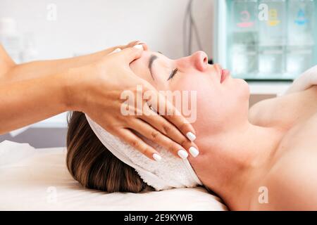 The cosmetologist massages the woman's face, preparing for the procedure. Portrait of the client and the doctor's hands in close-up. Side view. Concep Stock Photo