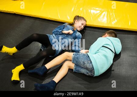Cute twin brother and sister jumping and bouncing on indoor trampoline together when spending time in children play center. Sports and entertainment Stock Photo