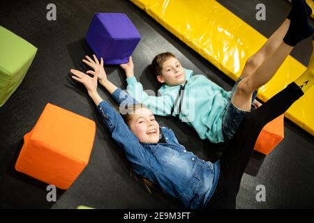 Cute twin brother and sister jumping and bouncing on indoor trampoline together when spending time in children play center. Sports and entertainment Stock Photo