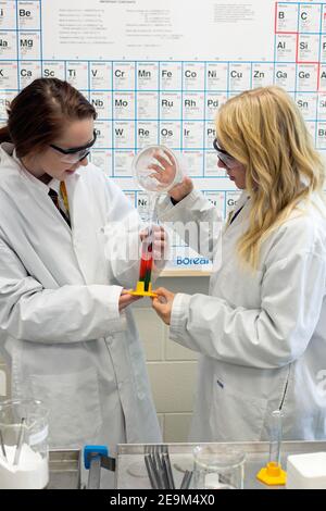 Two teenage female students performing a science experiment with periodic timetable in background. Stock Photo