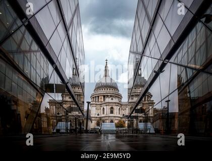 St Pauls Cathedral from low angle with leading lines and mirror reflections in glass as dramatic storm clouds gather above modern shopping centre
