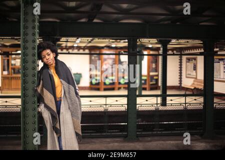 Shallow focus of a young African female with short curly hair waiting for a train in the station Stock Photo