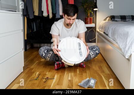 Young caucasian man doing cleaning for the holiday christmas in winter. A male in funny home clothes, pajamas with winter ornament collects and sets Stock Photo