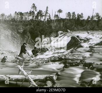 Two cowboys, possibly hunters as one has a rifle in his hand, sit at the edge of Haines Falls in the Catskill Mountains in Greene County, New York, in the 1880s Stock Photo