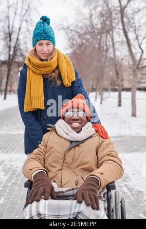 Portrait of African man sitting in wheelchair with his assistant behind his back they smiling at camera Stock Photo