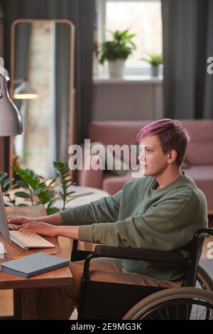 Disabled woman working as a freelancer at home sitting at the table and working on computer Stock Photo