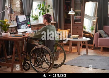 Rear view of disabled woman working as a programmer on computer with new software in domestic room Stock Photo