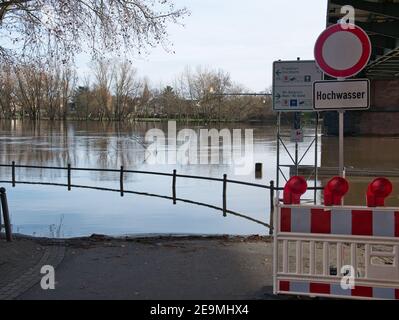 Warning sign warns of the flood by the river Main during the floods in 2021 near Mainz. Sign translation in front: 'Flooding'. Background: City names. Stock Photo