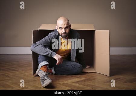 European male sitting by a cardboard box on the floor Stock Photo