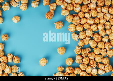 Popcorn is scattered on a blue background, in the form of a frame. Yummy for the filming of movies, TV series, cartoons. Free space, top view Stock Photo