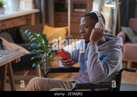 African man in headphones using his mobile phone while resting at home Stock Photo