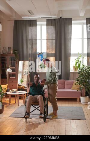 African man sitting on wheelchair and and doing exercises with his assistant at home Stock Photo