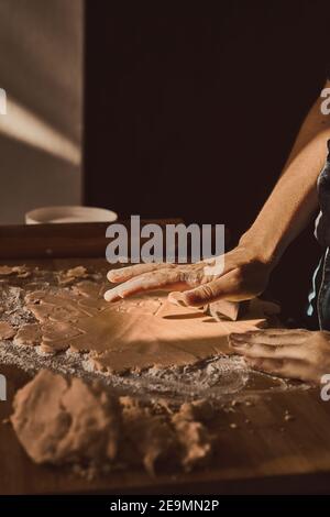 Woman's hand kneading the dough with a rolling pin on a wooden surface Stock Photo