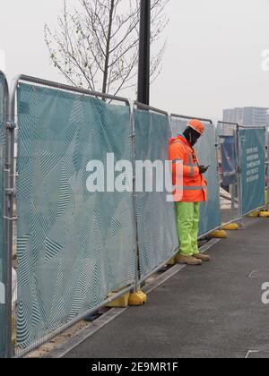 a construction worker in high viz clothes and hardhat looks at his mobile or cell phone Stock Photo
