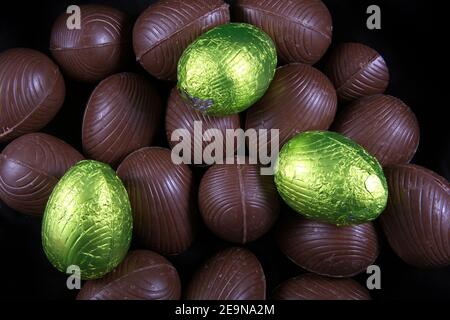 Pile of lime green or yellow foil wrapped & unwrapped chocolate easter eggs against a black background. Stock Photo