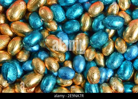 Blue,  gold and turquoise foil wrapped chocolate easter eggs, against a black background. Stock Photo