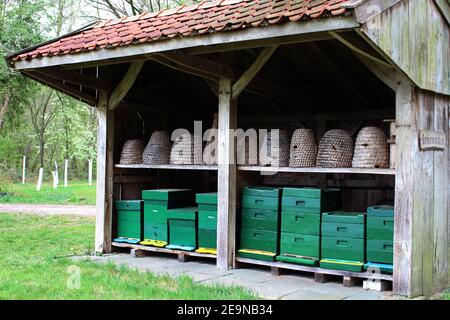 Reconstructed old fashioned bee barn for beekeeping. There are two rows of beehives in. Baskets and boxes. Bee skeps. Stock Photo