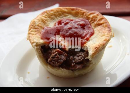 A traditional Australian meat pie with tomato sauce or ketchup Stock Photo